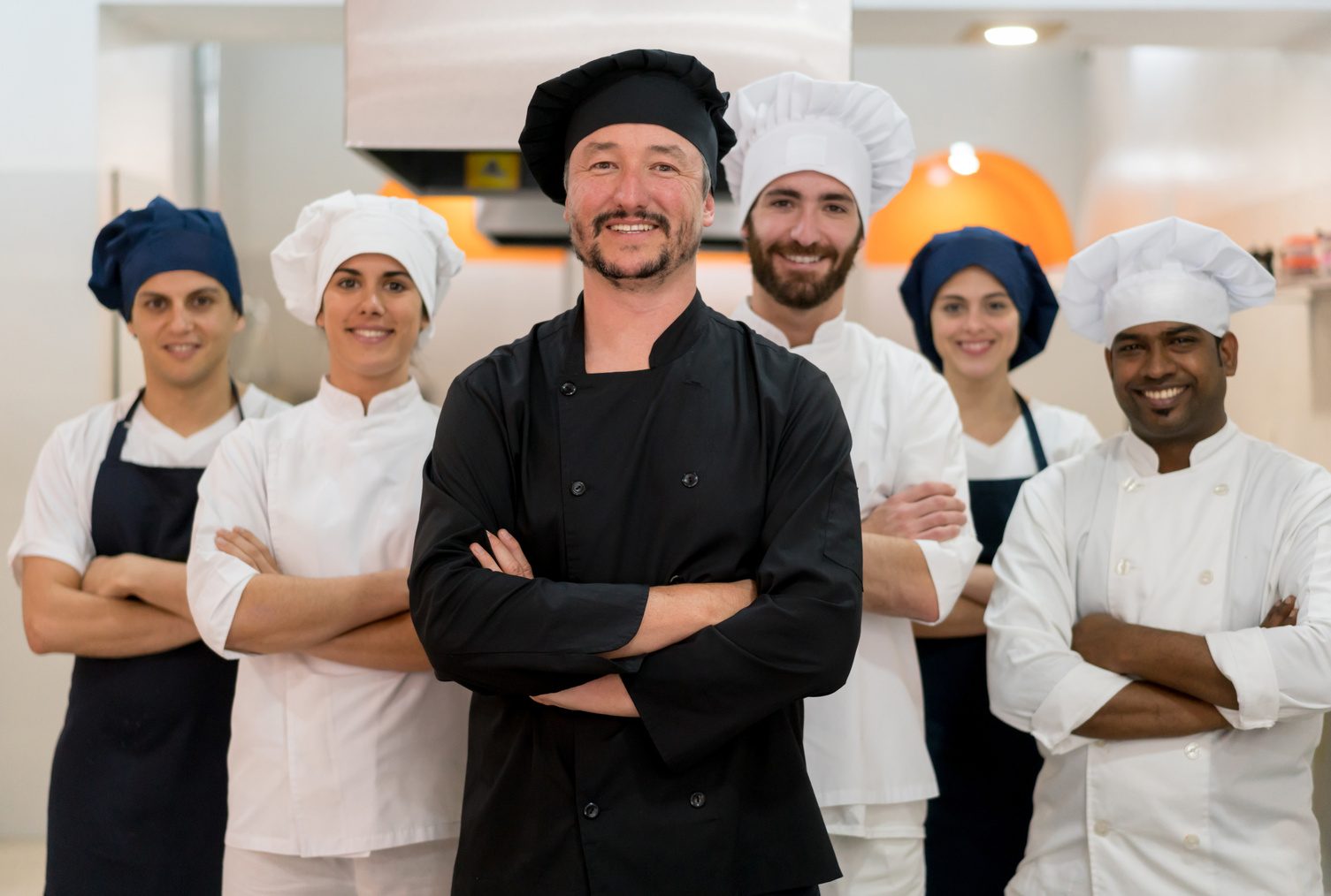 Proud team of chef, sous chefs and cooking assistants looking at camera smiling
