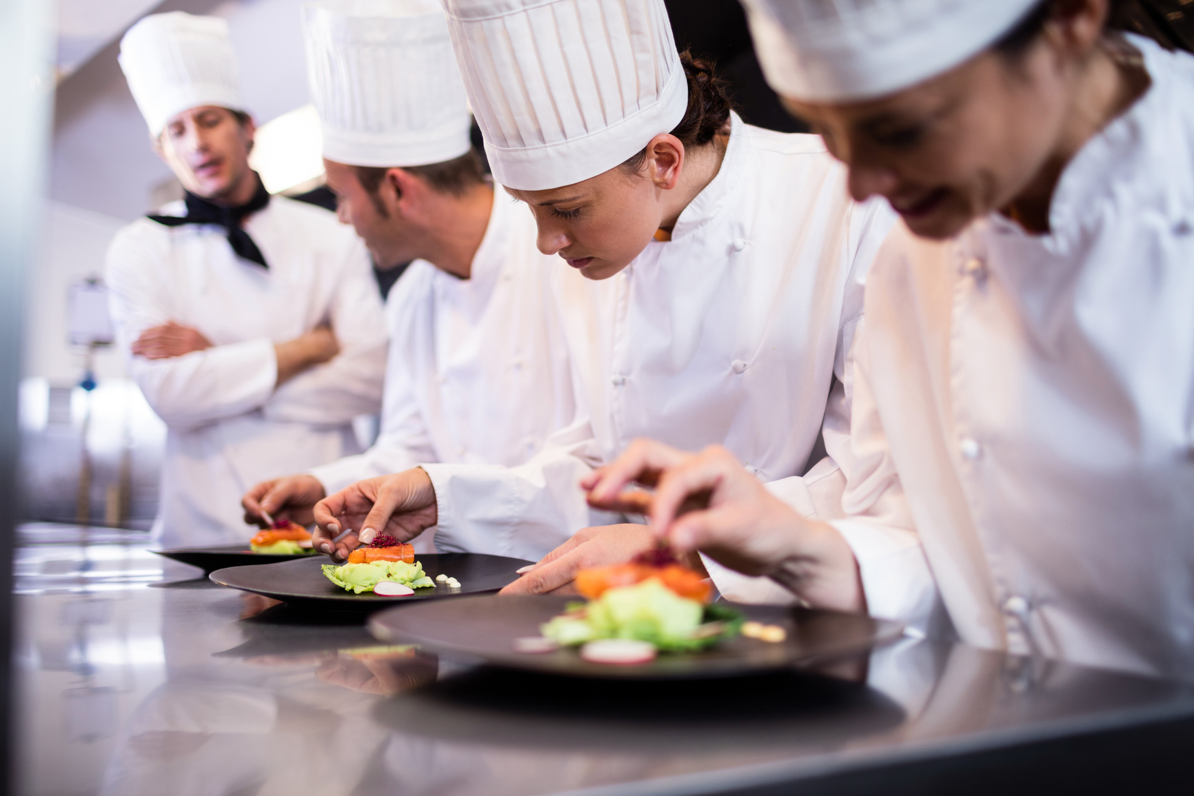 Head chef overlooking other chef preparing dish